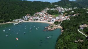 Vista aérea da Enseada de Ganchos, com a vila de pescadores na encosta, os barcos fundeados na enseada e o trapiche