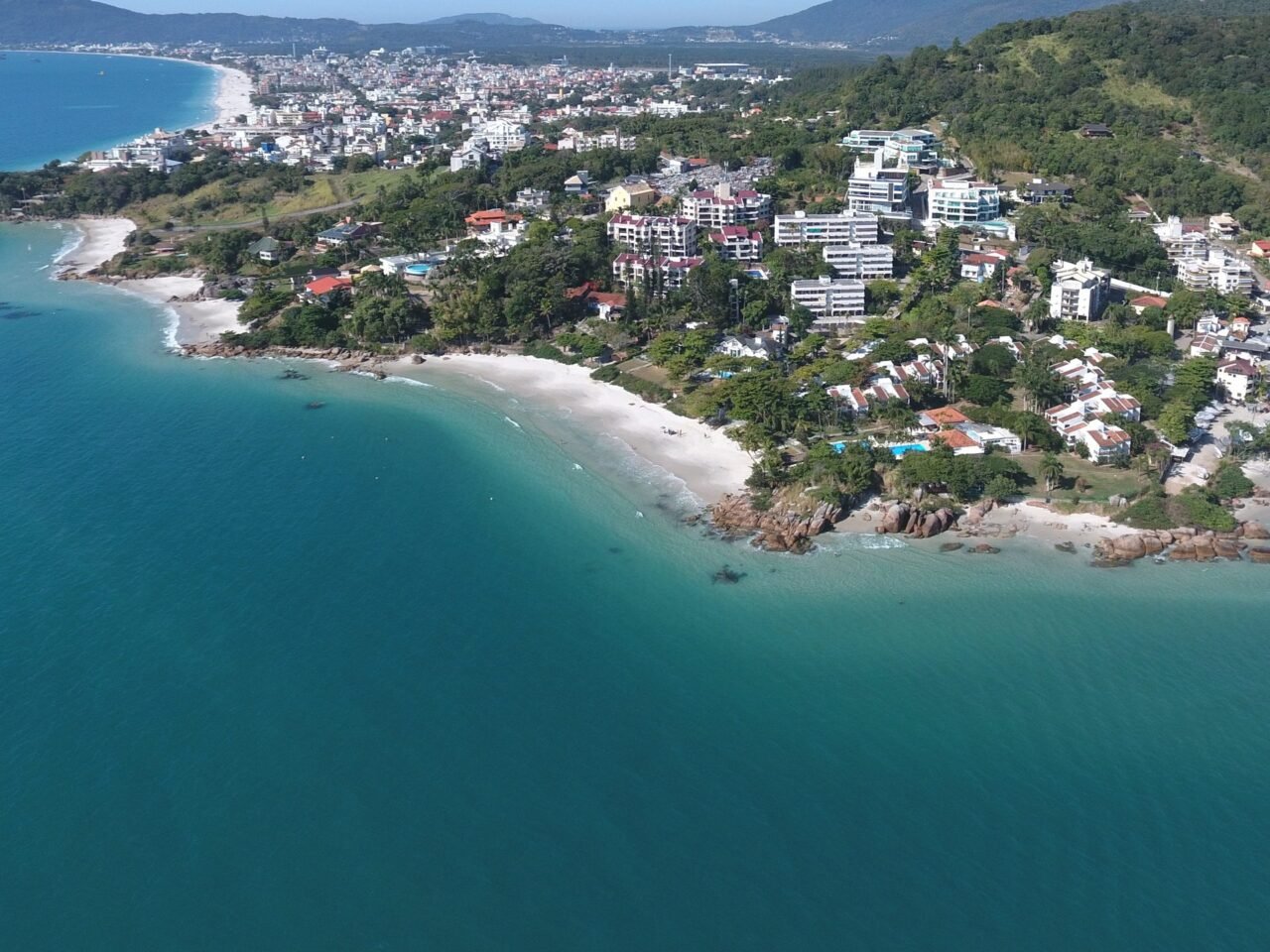 Vista aérea da Praia da Galega, com o costão de pedras na ponta e a faixa de areia entre a água clara e a encosta
